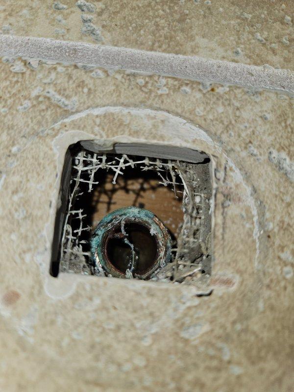 Accessed shower plumbing through cut access hole in tile to address pipe failure. Found corroded copper fitting with broken shower head and threads stuck inside eared ell. Replaced damaged 90-degree elbow fitting to restore proper shower functionality.