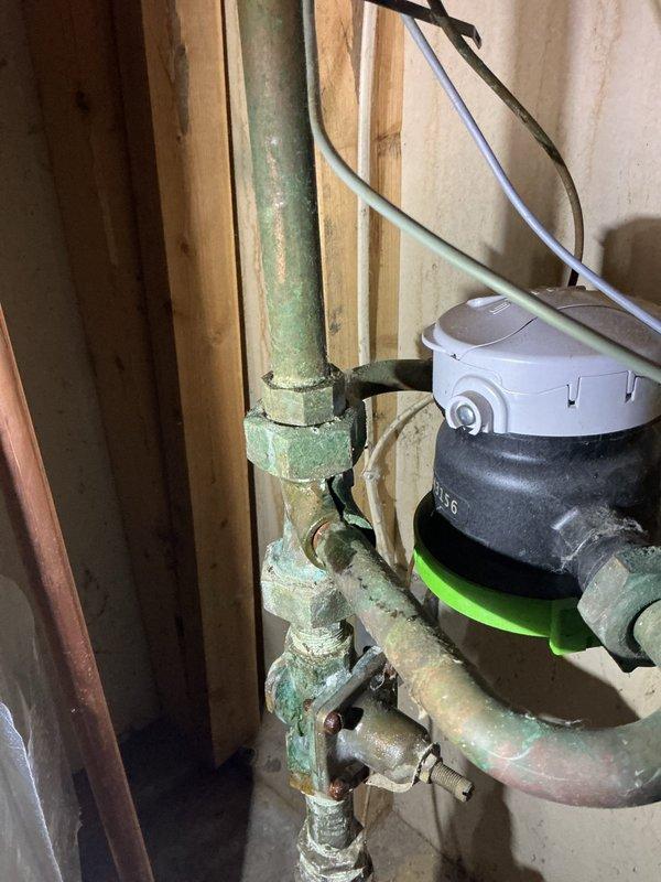 Responded to service call for a recurring water meter leak that had been previously serviced. Inspection revealed oxidized copper pipes with green patina and moisture at connection points. Tightened the affected fittings on the water meter assembly to stop the current dripping. Noted that if leakage continues, complete replacement of the affected components will be necessary.