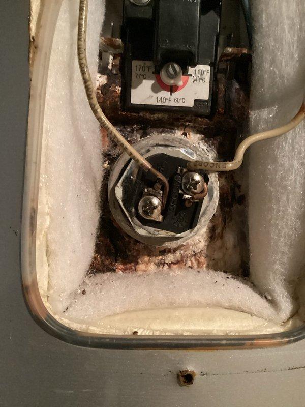 Inspected tanked water heater reported for no hot water issue. Discovered significant corrosion on thermostat housing and temperature control components with extensive rust deposits. Identified pin hole leak in tank causing water leakage. Recommended complete water heater replacement as repair not feasible due to tank integrity failure.