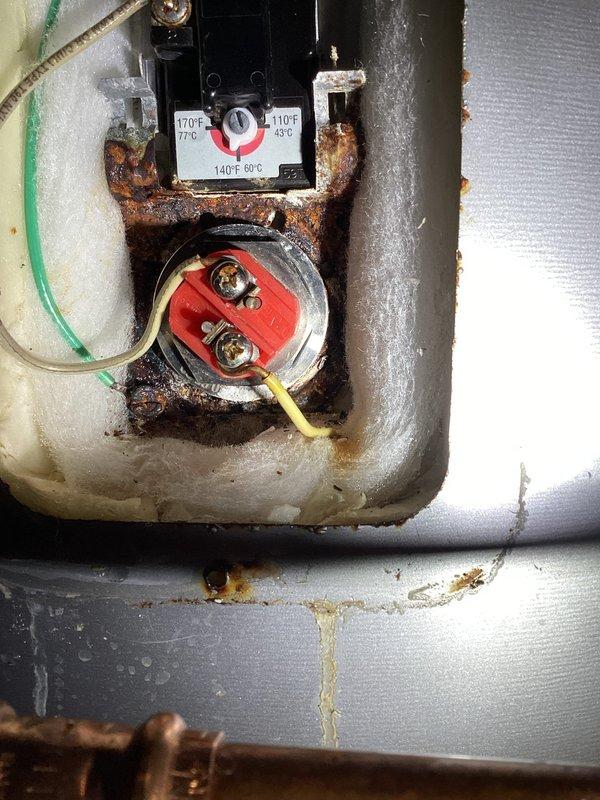 Inspected tanked water heater reported for no hot water issue. Discovered significant corrosion on thermostat housing and temperature control components with extensive rust deposits. Identified pin hole leak in tank causing water leakage. Recommended complete water heater replacement as repair not feasible due to tank integrity failure.