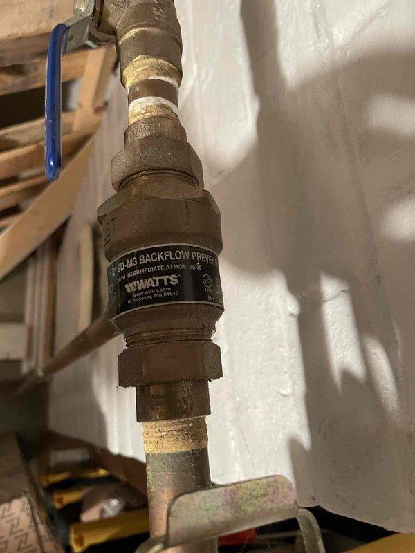 Responded to service call for boiler system with very low pressure. Determined auto fill valve was off, restored system pressure to 18 psi, and bled radiators throughout the property. Unable to bleed two radiators in living room due to inaccessible bleeders recessed into wall. Documented condition of aging backflow preventer valve and corrosion on heat exchanger components with photos.