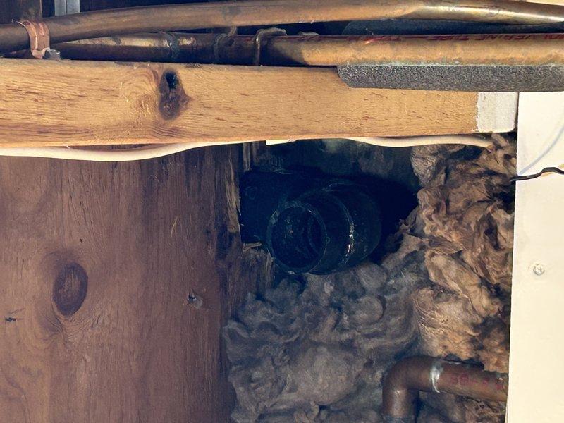Identified and repaired a leaking ABS T-fitting behind the wall that was causing water to penetrate from the kitchen sink to the lower level above the washing machine. Replaced damaged T-fitting and associated piping to resolve the leak, with visual inspection confirming proper drainage function through the newly installed PVC plumbing components.