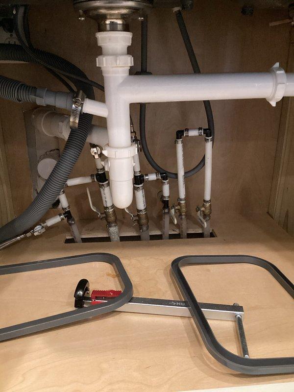 Conducted a comprehensive plumbing inspection of the water treatment system and under-sink plumbing components. Examined the water softener/filtration system with control valve assembly and associated PVC connections for proper installation and function. Inspected under-sink P-trap assembly, supply lines, shutoff valves, and drainage components, documenting the current condition with detailed photographs for reference.