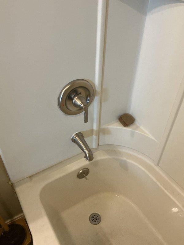 Responded to customer's request for revised shower faucet estimate after drywall removal. Upon inspection of the exposed wall cavity containing plumbing components and assessment of requirements, installed new shower valve with complete shower/tub trim. Completed installation includes brushed nickel/stainless steel control handle and curved tub spout in white bathtub/shower enclosure.