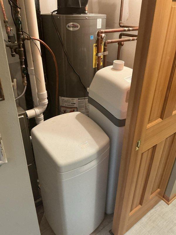 Responded to water leak report near customer's furnace. Inspected utility room containing Richmond water heater and dual water softener system with all connecting copper and PVC piping. Found no active leaks in the water treatment equipment or water heater installation during thorough examination of the mechanical room.