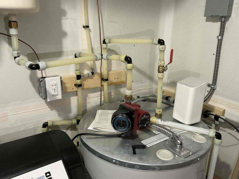Conducted comprehensive inspection of residential plumbing system, focusing on water heater installation with associated PVC piping network, valves, circulation pump, and connections. Also examined integrated HVAC components including BROAN ventilation unit, water softener system with digital controls, and wall-mounted expansion tank, confirming all systems are functioning within normal parameters.
