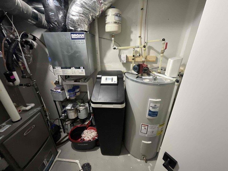 Conducted comprehensive inspection of residential plumbing system, focusing on water heater installation with associated PVC piping network, valves, circulation pump, and connections. Also examined integrated HVAC components including BROAN ventilation unit, water softener system with digital controls, and wall-mounted expansion tank, confirming all systems are functioning within normal parameters.