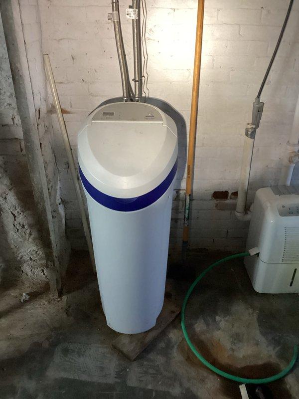 Conducted comprehensive plumbing inspection of residential property, examining toilet flush mechanism components which showed normal wear but appeared functional. Inspected water softener system and associated plumbing connections in basement area, noting proper installation with no visible leaks, while also observing adjacent dehumidifier setup with drainage hose.
