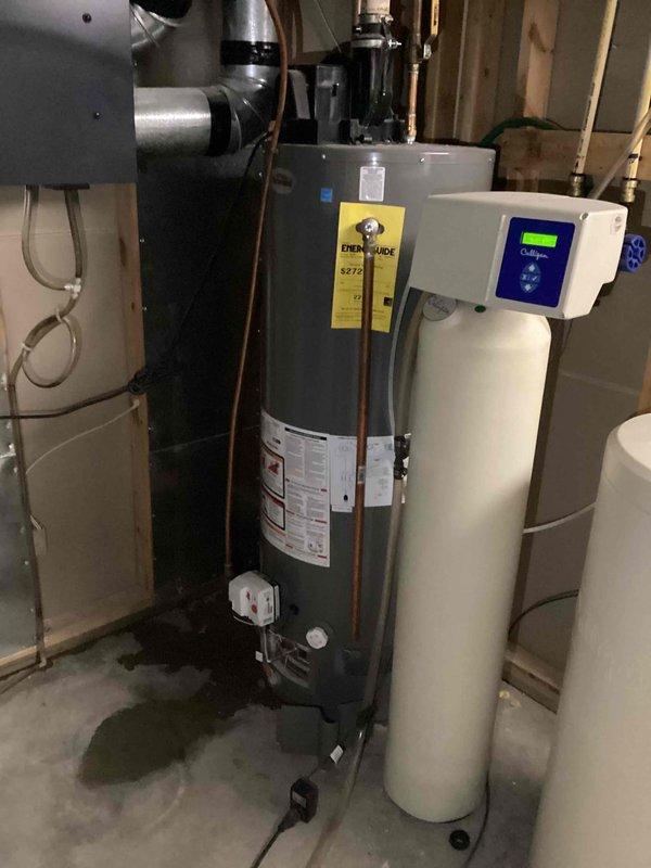 # Service Report: Water Heater Replacement Assessment

Responded to service call for 10-year-old Richmond 50-gallon natural gas power vent water heater with active leak. Upon inspection, confirmed internal tank failure with visible water leakage from bottom of unit and evidence of water staining on concrete floor beneath heater. Identified outdated cellular core venting system that does not meet current code requirements. Documented equipment condition with photographs showing water heater, associated plumbing connections, and surrounding mechanical systems including water treatment equipment. Provided comprehensive replacement estimate to address failed water heater and bring venting system up to current standards.