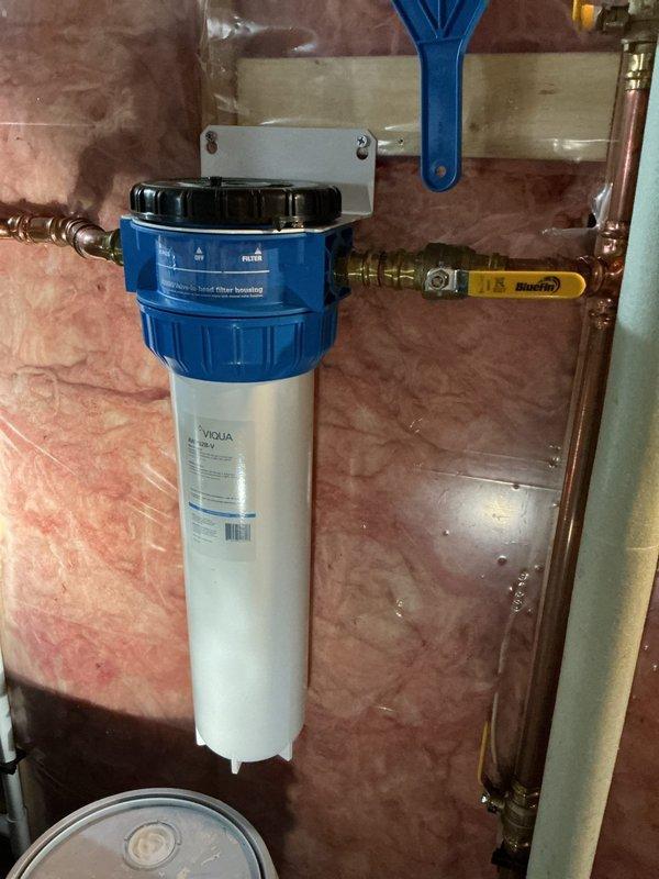 Completed comprehensive plumbing inspection of residential property including bathroom fixtures and water treatment system. Inspected bathtub, shower controls, tub spout, and tiled surround—all fixtures operating properly with no leaks or deficiencies noted. Examined whole-house water filtration system with VIQUA filter housing, copper piping connections, compression fittings, and isolation valve; system functioning correctly with no service requirements. No corrective action needed.