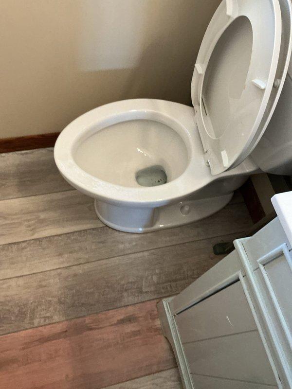 Responded to service call for toilet backup and water leakage at base. Upon inspection, determined toilet was experiencing backup when shower was running, causing water to overflow from toilet base onto bathroom floor. Diagnosed issue as main drain line blockage beneath floor rather than toilet-specific problem. Recommended professional drain cleaning service to clear main sewer line obstruction. Advised customer that toilet would need to be removed and reset after drain line is cleared, and offered to return for toilet reinstallation if needed.