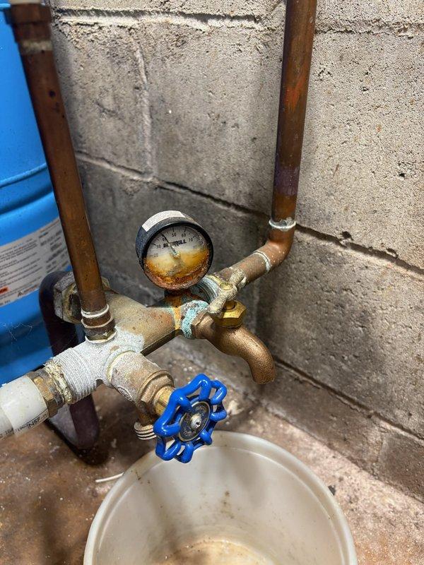 Responded to service call for copper oxidation and blue-green buildup on plumbing fixtures in unfinished basement near well system. Inspected copper piping, brass fittings, gate valves, and pressure gauge showing significant corrosion and mineral deposits. Documented corroded tank tee, rusted pressure tank with water staining at base, and compromised copper connections throughout well assembly. Photographed existing conditions and scheduled follow-up assessment for complete repipe evaluation and pressure tank tee replacement to address ongoing water quality issues affecting copper components.