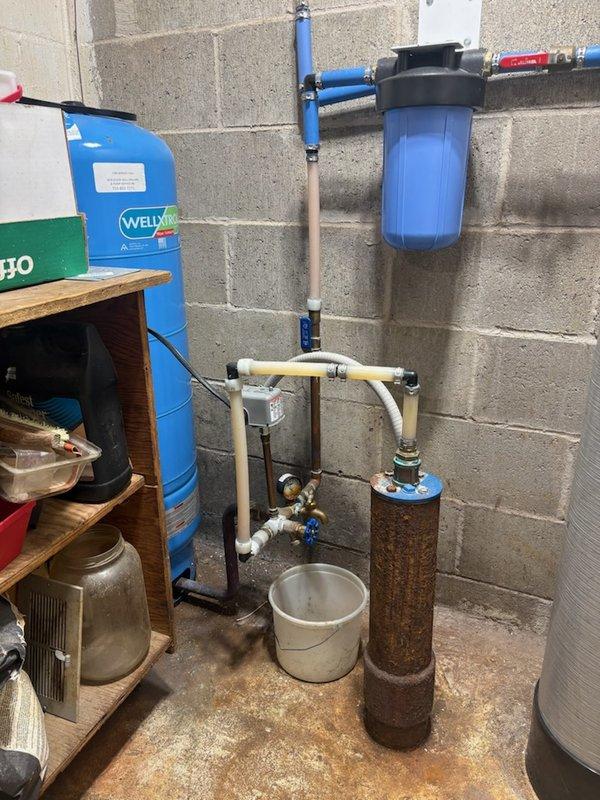 Responded to service call for copper oxidation and blue-green buildup on plumbing fixtures in unfinished basement near well system. Inspected copper piping, brass fittings, gate valves, and pressure gauge showing significant corrosion and mineral deposits. Documented corroded tank tee, rusted pressure tank with water staining at base, and compromised copper connections throughout well assembly. Photographed existing conditions and scheduled follow-up assessment for complete repipe evaluation and pressure tank tee replacement to address ongoing water quality issues affecting copper components.