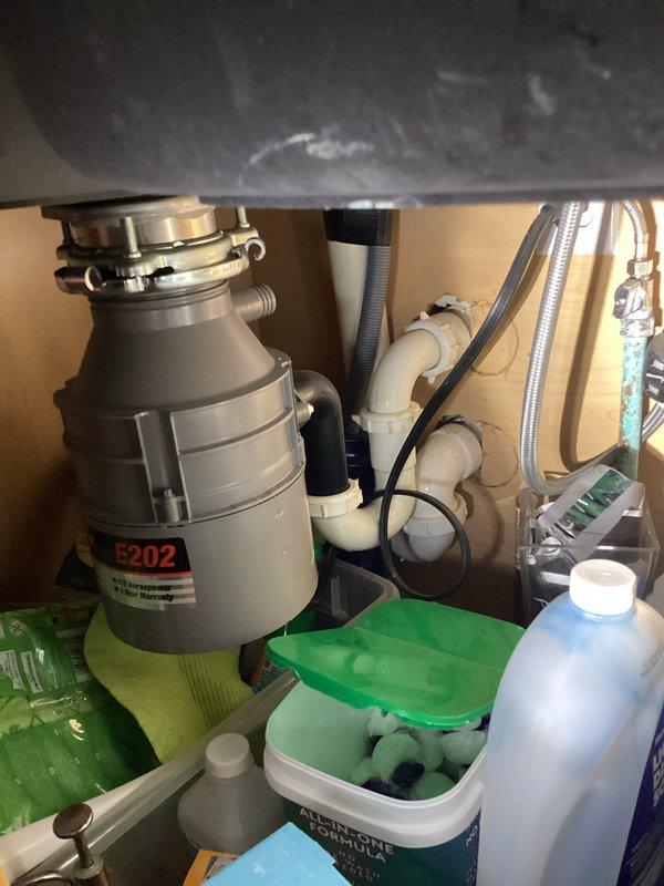 Completed comprehensive plumbing inspection of residential kitchen fixtures and under-sink plumbing system. Verified proper operation of chrome pull-down faucet, examined garbage disposal unit (model E202) with connected PVC drain lines and flexible supply lines, and confirmed all components were functioning correctly with no visible leaks or deficiencies noted.