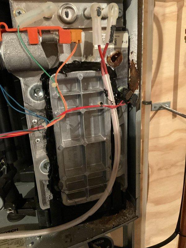 Responded to repeat service call for boiler displaying EA error code and flame failure condition. Upon inspection, found flame sensor severely deteriorated and nearly disintegrated, with spark electrodes also showing advanced wear. Discovered heat exchanger cleanout cover leaking exhaust gases into cabinet due to seized mounting bolt that cannot be properly tightened. Applied high-temperature silicone as temporary measure to maintain operation for domestic hot water needs. Removed and inspected flame sensing components, confirming replacement required. Submitted parts information to verify warranty coverage for heat exchanger, flame sensor, and ignitor assembly. Unit requires complete heat exchanger replacement for permanent repair; temporary measures implemented to maintain safe operation pending customer decision on repairs.