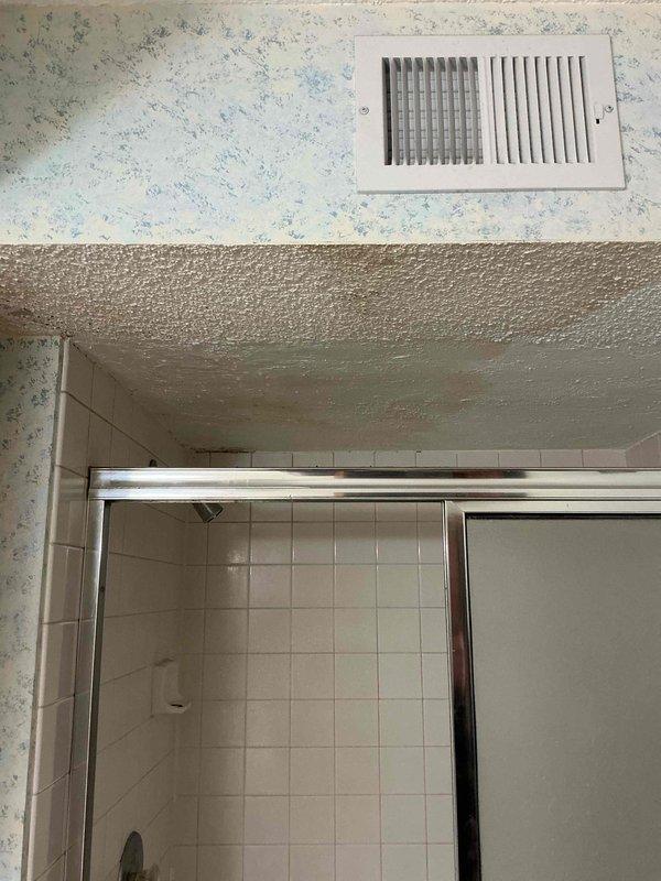 Responded to emergency water leak with water actively penetrating ceiling from bathroom above. Upon arrival, main water supply had been shut off to prevent further damage. Conducted thorough inspection of bathroom area, including ceiling cavity, ventilation systems, and shower enclosure to identify leak source. Documentation photos captured ceiling damage, wallpaper water staining, textured ceiling deterioration, and shower door assembly configuration. Assessment determined extensive sheetrock removal would be required to access plumbing lines and complete repairs. Coordinated with restoration company for water damage mitigation and structural drying before plumbing repairs can proceed.
