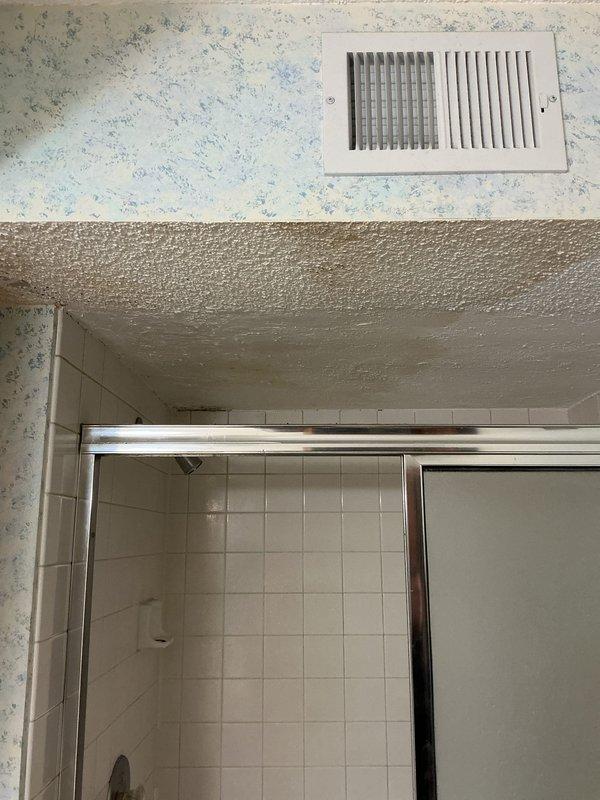 Responded to emergency water leak with water actively penetrating ceiling from bathroom above. Upon arrival, main water supply had been shut off to prevent further damage. Conducted thorough inspection of bathroom area, including ceiling cavity, ventilation systems, and shower enclosure to identify leak source. Documentation photos captured ceiling damage, wallpaper water staining, textured ceiling deterioration, and shower door assembly configuration. Assessment determined extensive sheetrock removal would be required to access plumbing lines and complete repairs. Coordinated with restoration company for water damage mitigation and structural drying before plumbing repairs can proceed.