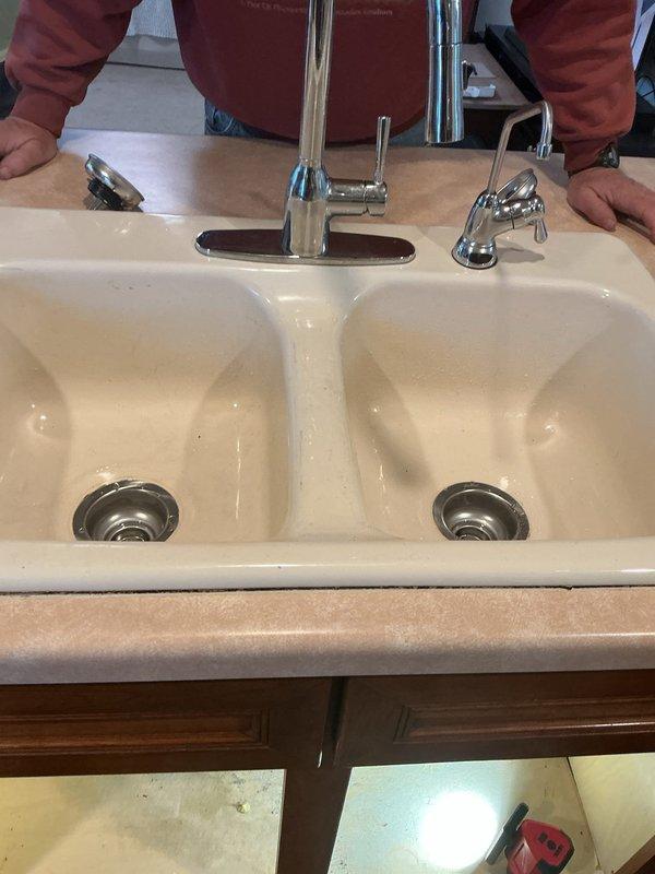 Reinstalled complete plumbing assembly underneath double-basin kitchen sink following previous removal. Reconnected water supply lines and drain system, including P-trap configuration, white PVC drain lines, and garbage disposal unit with associated discharge piping. Verified all connections secure, tested system for proper drainage and confirmed no leaks present.