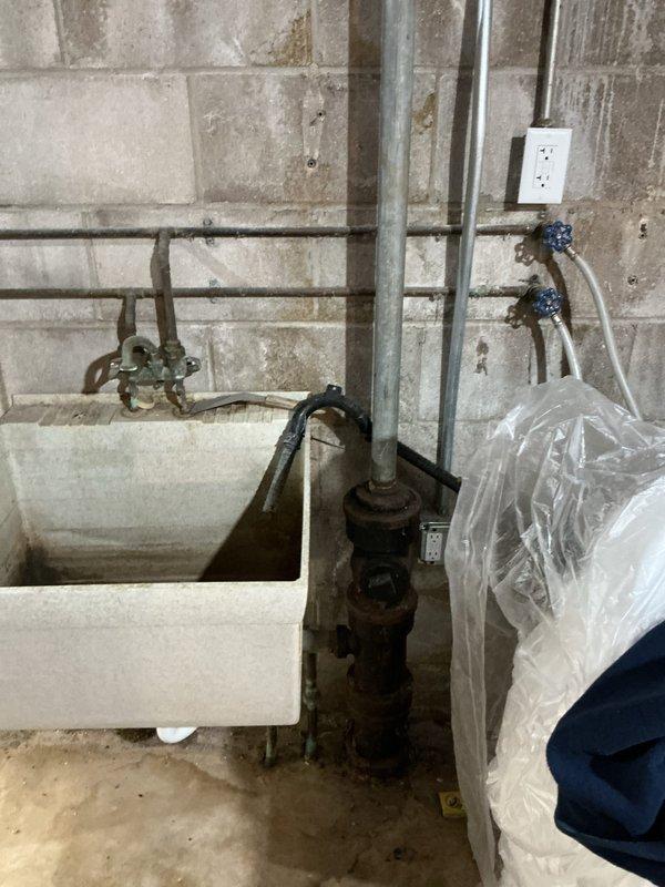 Relocated existing Ruud tanked water heater and temporarily reconfigured plumbing system to accommodate basement drainage tile installation by separate contractor. Disconnected and capped laundry tub drain, removed utility sink, and relocated multiple water supply lines to clear work area while maintaining active water service to residence. Re-piped water heater connections with copper piping to new temporary location, ensuring all connections remained functional and code-compliant during drainage work phase.