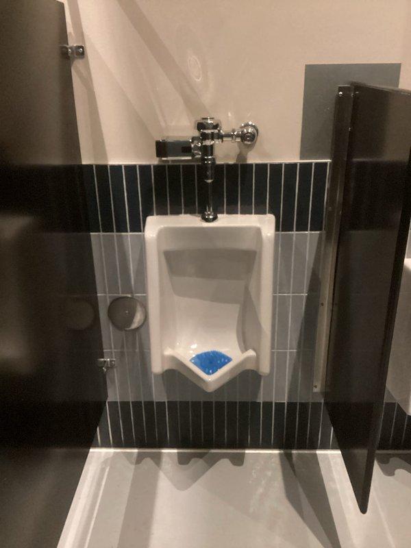 Responded to emergency call for overflowing wall-mounted urinal in commercial restroom facility. Upon arrival, confirmed water supply had been shut off to prevent further leaking. Performed diagnostic assessment and identified blockage in urinal drain line caused by mineral buildup and debris accumulation. Utilized drain cable equipment to clear obstruction from the line, restoring proper drainage and flow. Tested flush valve operation and verified complete clearance of blockage. Restored water supply and conducted final operational test to ensure urinal was functioning properly without leaks.