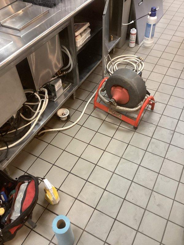Responded to main drain backup in commercial kitchen facility. Floor drain beneath refrigeration equipment was clogged with syrup buildup. Used cable machine to clear blockage and restore proper drainage. Previous service had been performed for similar issue, indicating recurring problem with syrup disposal in this location.