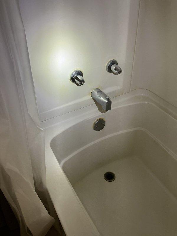 Responded to water leak complaint in shower unit. Upon inspection, identified active leak occurring at back end of shower liner during operation. Traced source to shower valve assembly and discovered pinhole leak in valve body. Documented existing conditions with photographs showing white fiberglass tub/shower combination unit with three-handle chrome fixture configuration and evidence of water infiltration. Provided estimate for shower valve replacement to resolve leak issue.