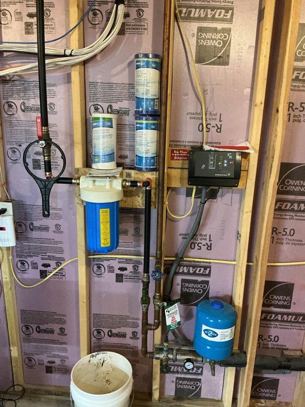 Completed comprehensive plumbing inspection of residential property. Successfully repaired malfunctioning faucet located adjacent to sauna room, restoring proper water flow and function. Documented existing water filtration and treatment system installation, including three-stage filter cartridge assembly, pressure expansion tank, and associated copper and PVC plumbing connections within exposed wall framing.