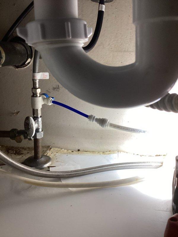 Responded to emergency water leak under kitchen sink caused by pinhole leak in 3/8" push fit supply line. Main water supply had been shut off by homeowner due to active spraying. Replaced defective stop valve and damaged section of 3/8" supply line with new components. Restored water service and verified all connections for proper operation with no leaks detected.