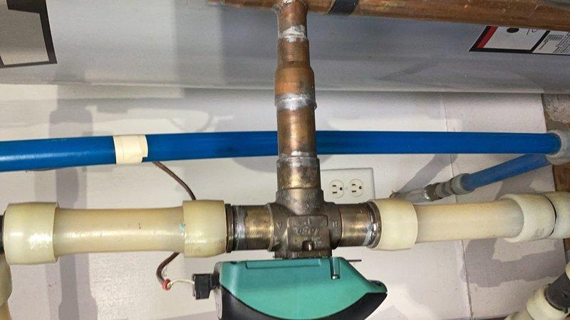 Responded to service call for central boiler system experiencing overheating condition with home temperature reaching 80+ degrees. Diagnosed malfunctioning three-way zone valve that was stuck open and failing to shut off completely, causing unintended heat bypass to the baseboard radiators from the woodstove heating system. The defective sweat valve was allowing continuous hot water circulation to the radiators regardless of thermostat settings. Provided estimate for replacement of the faulty three-way valve with new unit to restore proper zone control and prevent continued overheating. Customer approved repair work to be scheduled at next available opportunity. Documented existing plumbing configuration including mixed piping materials (copper, PEX, and CPVC) and current valve assembly with photos for reference during upcoming valve replacement.