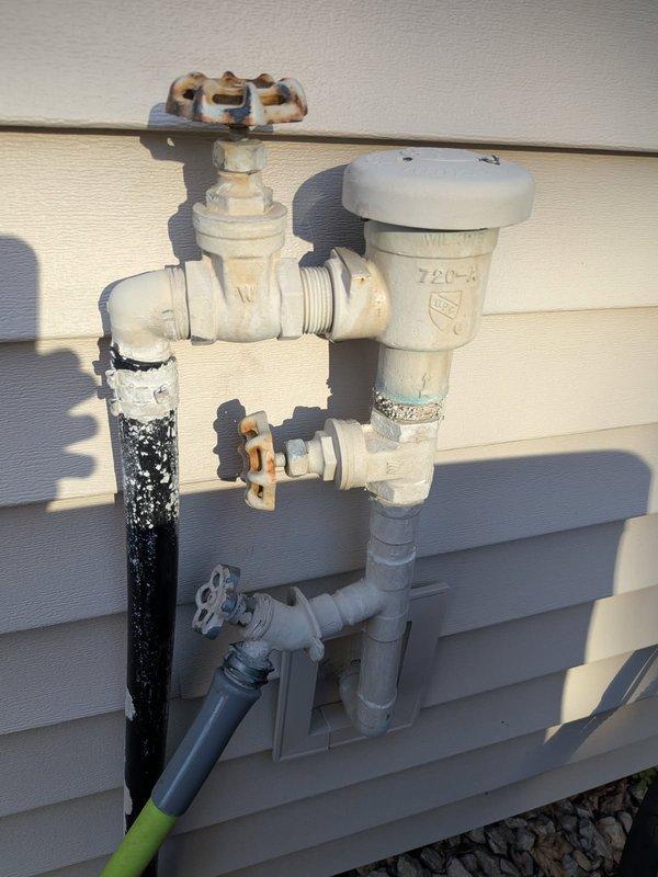 Responded to irrigation system leaks at outdoor spigot assembly with multiple failure points. Upon inspection, identified failed vacuum breaker (model 720-A), corroded gate valve shutoff, and compromised frost-proof hose bib with active leaking at seal points. Water was being temporarily redirected through attached hose to prevent foundation damage. Assessed entire plumbing assembly mounted on exterior wall, noting significant rust and corrosion on metal valve components and deteriorated connection points. Shut off affected components to stop active water loss. Scheduled return visit to replace irrigation vacuum breaker, shutoff valve, and install new frost-proof hose bib assembly to restore proper function and prevent future leaks.