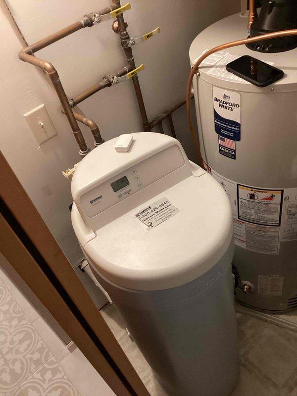 Responded to service call for water softener not using salt and producing no soft water. Upon inspection, found 10-year-old water softener unit with digital control panel showing operational issues. Evaluated system including copper piping connections, shut-off valves, and bypass configuration. Assessed water softener's mechanical and electronic components to determine failure point preventing salt consumption and regeneration cycle. Documented equipment condition with photographic evidence of plumbing connections, control head, and overall system layout. Recommended advisor consultation for comprehensive system evaluation and replacement options due to age and condition of existing unit.