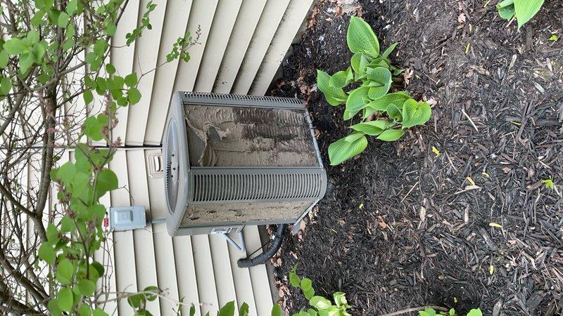 Performed comprehensive AC tune-up on outdoor condensing unit, including cleaning and inspection of all components. Unit showed signs of age with accumulated debris on top surface and surrounding area; removed organic matter and cleaned exterior housing. Verified proper operation of cylindrical barrel-style condenser with horizontal ribbed fins, checked refrigerant levels, inspected electrical connections, and confirmed adequate airflow through ventilation grilles. Noted dryer vent positioned in close proximity to AC unit and verified proper clearance for system operation. All components functioning within normal parameters upon completion of maintenance service.