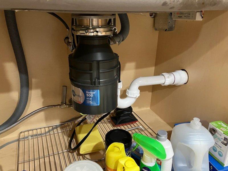 Completed installation of customer-supplied Kohler pull-down kitchen faucet and Badger 500 garbage disposal unit. Removed existing fixtures, installed new disposal with proper mounting assembly and drain connections, connected corrugated drain hose with secure metal clamps, and configured white PVC P-trap drainage system to code. All connections tested for proper operation and leaks, with no issues detected upon completion.