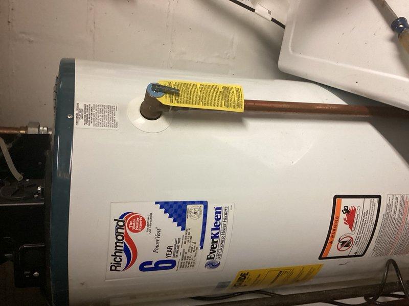 Responded to no hot water complaint for residential property with new infant. Upon inspection, found 19-year-old Richmond brand tanked water heater installed in utility area. Unit had exceeded typical service life expectancy and was no longer producing hot water. Assessed burner assembly and overall system condition. Provided estimate for burner cleaning service as well as complete water heater replacement options given the advanced age of existing equipment. Documented current installation configuration including copper supply piping, gas valve assembly, and drain pan placement for replacement planning purposes.