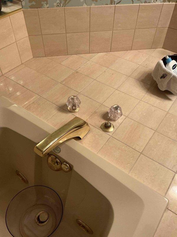 Responded to service call for leaking bathroom fixtures including a Roman tub spigot and vanity faucet with dripping issues. Upon inspection, identified failed cartridge in the Roman tub faucet and oversplashing condition at the vanity sink with gold-finished fixtures and crystal knob handles. Provided estimate for cartridge replacement on both fixtures and performed cleaning of the tiled countertop surface to remove water deposits and staining.