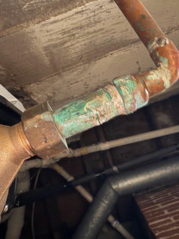 Responded to multiple water leak emergency behind furnace and water heater. Upon inspection, identified three separate leak sources: corroded copper fitting behind water heater, failed water meter spud connection, and deteriorating gate valve above furnace. The copper piping exhibited extensive corrosion with green verdigris and white mineral deposits indicating long-term moisture exposure and oxidation damage. Documented all leak locations with photographs showing the severity of deterioration on the copper pipes and brass fittings. Provided estimate for replacement of the water meter spud and removal of the compromised gate valve to resolve the active leaks and prevent further water damage to the mechanical room.