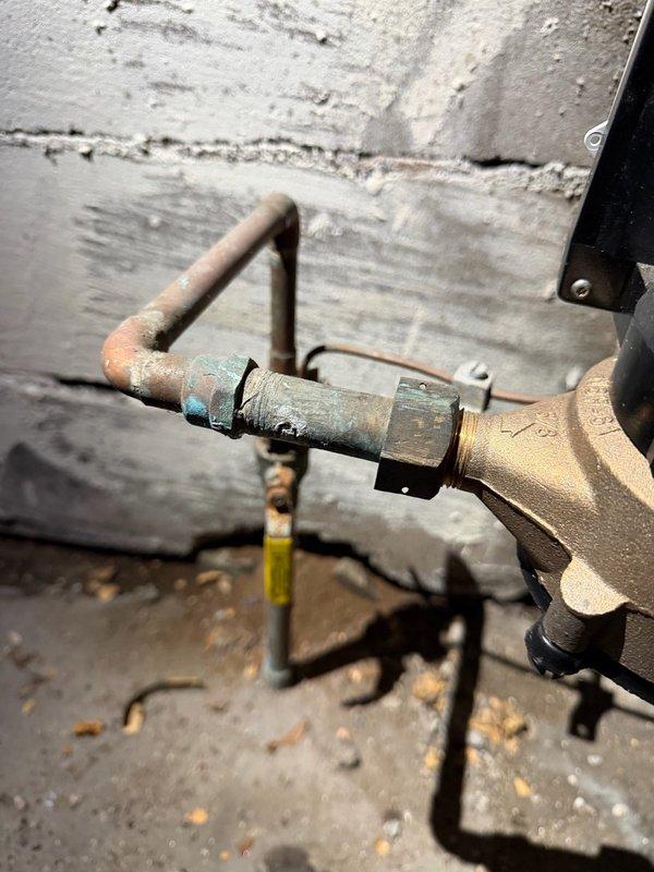 Responded to multiple water leak emergency behind furnace and water heater. Upon inspection, identified three separate leak sources: corroded copper fitting behind water heater, failed water meter spud connection, and deteriorating gate valve above furnace. The copper piping exhibited extensive corrosion with green verdigris and white mineral deposits indicating long-term moisture exposure and oxidation damage. Documented all leak locations with photographs showing the severity of deterioration on the copper pipes and brass fittings. Provided estimate for replacement of the water meter spud and removal of the compromised gate valve to resolve the active leaks and prevent further water damage to the mechanical room.