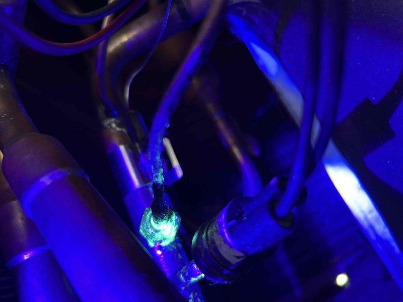 Responded to no cooling complaint on 5-year-old residential air conditioning unit blowing warm air. System was low on refrigerant charge for the second consecutive year, indicating ongoing leak. Performed UV dye leak detection and identified fluorescent dye accumulation at the suction line connection nut at the outdoor thermostatic expansion valve (TXV). Due to limited access and lack of appropriately sized wrench on truck, unable to attempt tightening the connection to determine if leak is repairable at the fitting or if complete TXV replacement is required. Submitted parts order request and initiated warranty inquiry given unit age. Customer advised that parts department will research warranty coverage and provide repair pricing options for follow-up service appointment to complete permanent repair.