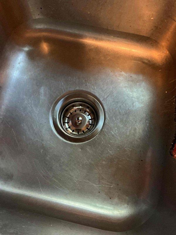 Responded to service call for kitchen sink leak and drainage issues. Upon inspection, identified failed kitchen sink strainer as source of leak beneath sink. Additionally diagnosed backing up drains throughout property caused by mainline sewer blockage, which required coordination with separate sewer service contractor. Replaced defective kitchen sink strainer and continuous waste assembly to resolve leak. Documented existing conditions with photographs showing worn strainer and sink basin prior to replacement. Communicated findings regarding mainline sewer backup to property owner for separate remediation.