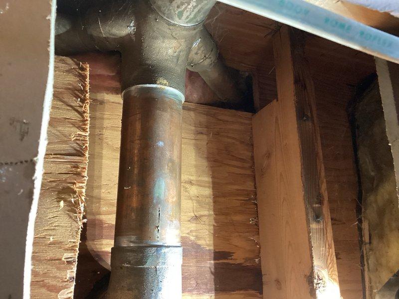 Responded to a water leak originating from the upstairs toilet and manifesting in the downstairs ceiling. Upon inspection, identified a compromised copper supply line between the toilet closet flange connection and the drain assembly, specifically at the section between the toilet 90-degree elbow and double wye fitting. The copper pipe exhibited significant corrosion and blue-green patina indicative of long-term moisture exposure and oxidation. Documented the condition of the affected plumbing infrastructure with photographs showing the deteriorated copper piping within the floor joist cavity. Coordinated with repipe specialist for comprehensive assessment and replacement estimate of the damaged water supply line.