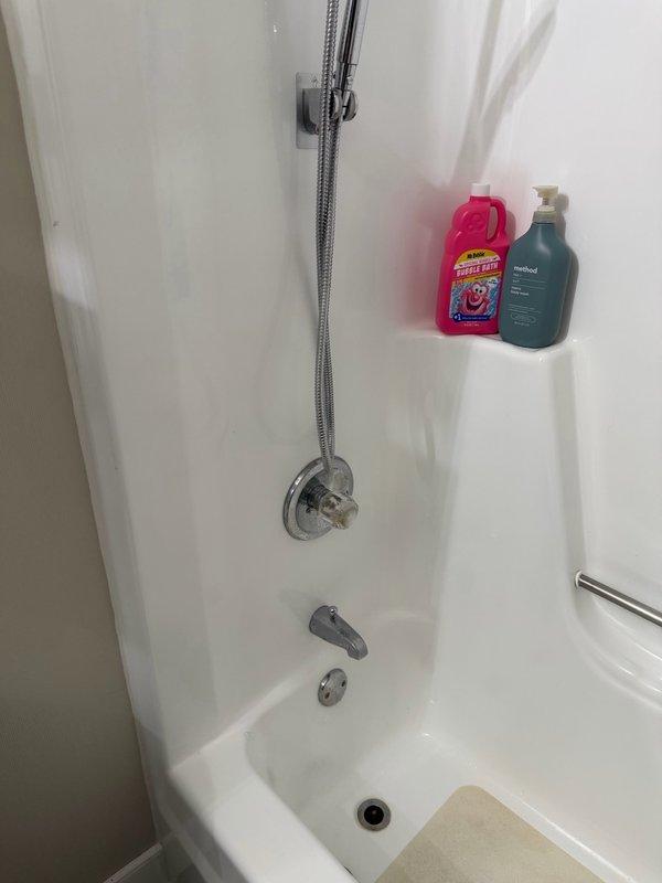 Responded to report of bathtub drain leaking through ceiling. Upon arrival, performed diagnostic testing by running water through tub drain assembly—no leakage detected at drain connection. Conducted systematic water testing at tub spout, overflow assembly, and shower valve trim. Testing revealed water infiltration occurring at back side of shower wall, indicating compromised seal at fixture penetrations. Applied silicone sealant around all tub trim components and along back side of shower wall to prevent further water intrusion. Documented conditions with photographs of shower assembly and accessible plumbing connections in ceiling space below.