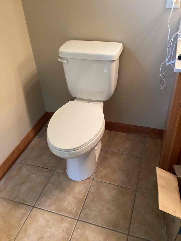 Installed new ADA-compliant comfort height toilet in residential bathroom, replacing existing fixture. Installation included new wax ring seal and mounting bolts to ensure proper connection to the waste flange. Completed basic installation with toilet properly secured and positioned against wall in corner location, verified proper function and seal integrity.