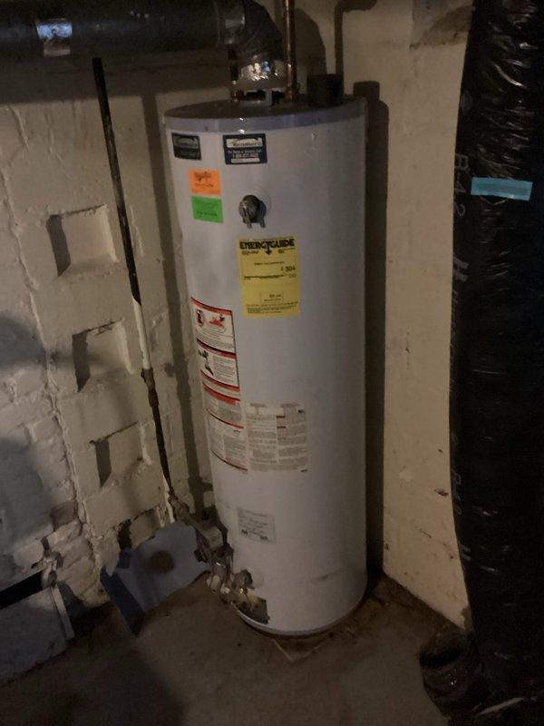 Responded to no hot water complaint and performed biannual plumbing maintenance inspection. Upon arrival, found pilot light extinguished on water heater located in basement utility area. Conducted thorough assessment of water heating system, including examination of gas valve assembly, thermostat controls, and all piping connections. Inspected age and condition of existing white cylindrical water heater unit with visible copper and black pipe fittings at top connections. 

During preventive maintenance evaluation, identified that water heater is no longer maintaining proper temperature settings despite pilot light status. Unit displays significant age-related degradation affecting heating performance and temperature consistency. Documented current condition with photographs showing EnergyGuide label, manufacturer specifications, control valve assembly, and overall installation configuration against painted concrete block wall. Noted standard plumbing connections including copper supply