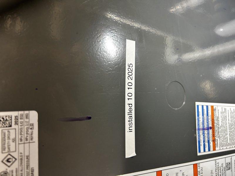 Responded to no cooling complaint on one-year-old Goodman system running continuously. Inspected indoor coil and confirmed no freeze-up, though evidence of water on floor indicated previous freezing condition. Connected manifold gauges and found near-zero suction pressure and low liquid line pressure. Identified active refrigerant leak at outdoor unit Schrader valve, documented with video evidence. Performed bubble test on all accessible refrigerant connections with no additional leaks detected. System confirmed low on R32 refrigerant. Scheduled follow-up visit to replace leaking Schrader valve and recharge system with R32 refrigerant once pricing and materials are obtained.
