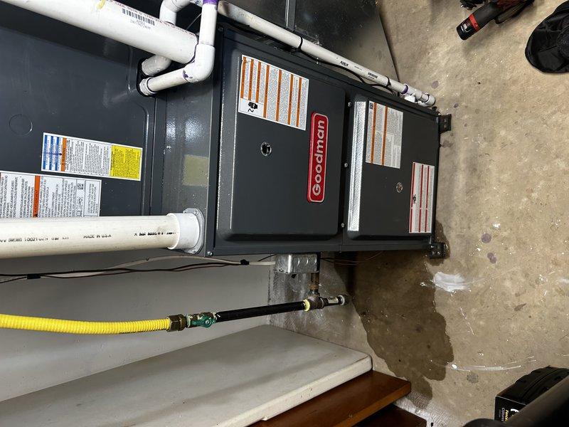 Responded to no cooling complaint on one-year-old Goodman system running continuously. Inspected indoor coil and confirmed no freeze-up, though evidence of water on floor indicated previous freezing condition. Connected manifold gauges and found near-zero suction pressure and low liquid line pressure. Identified active refrigerant leak at outdoor unit Schrader valve, documented with video evidence. Performed bubble test on all accessible refrigerant connections with no additional leaks detected. System confirmed low on R32 refrigerant. Scheduled follow-up visit to replace leaking Schrader valve and recharge system with R32 refrigerant once pricing and materials are obtained.