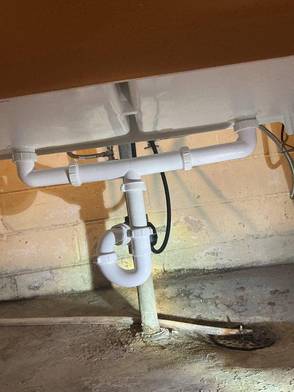 Responded to water leak at laundry tub fixture with leaking observed from right-hand side connections. Upon inspection, discovered PVC drain connections had been assembled dry without proper lubrication, causing water seepage at joints. Disassembled affected drain assembly, applied appropriate pipe lubricant to all connection points, and reassembled P-trap and tailpiece connections to manufacturer specifications. Verified all joints were properly sealed and tested system for leaks. Photographed completed plumbing assembly showing proper installation of white PVC drain configuration with secured mounting clips.