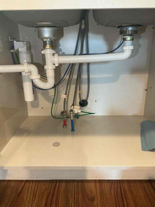 Responded to kitchen sink leak originating from cabinet area. Upon inspection, identified severely leaking basket strainer with stripped mounting nut that could not be properly tightened. The compromised basket strainer assembly was causing water discharge into the cabinet below the double-basin stainless steel sink. Assessed the damaged hardware and plumbing configuration, including existing PVC drain lines and P-trap connections serving both sink basins.