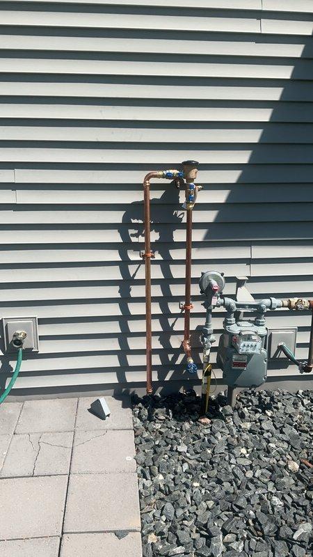 Installed new irrigation line by running copper piping from basement through exterior wall to outside of building. Installed pressure vacuum breaker on exterior wall per code requirements to prevent backflow contamination of potable water supply. All work completed in accordance with municipal plumbing permit specifications, with copper pipe properly secured and all connections soldered and pressure tested for leaks.
