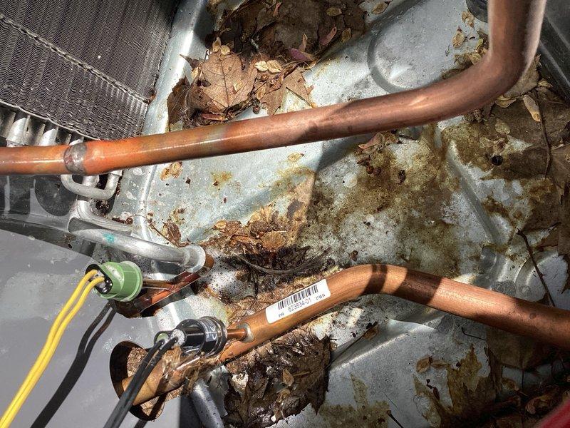 Responded to no cooling complaint on 8-month-old air conditioning system experiencing inadequate temperature reduction. Upon inspection, found unit operating with low refrigerant charge. Performed comprehensive leak detection procedures and identified active refrigerant leak at condensing coil. Photographic documentation captured severe corrosion on copper tubing with visible oxidation and surface degradation, along with frost accumulation on coil fins indicating restricted airflow and moisture exposure issues. Drain pan showed significant staining, organic debris accumulation, and evidence of prolonged moisture exposure. Temporarily recharged system to restore immediate cooling function; however, advised that this is a short-term solution as refrigerant will continue leaking. Strongly recommended immediate condensing coil replacement or full unit replacement given the age of equipment and severity of coil deterioration. Unit requires urgent attention to prevent complete system failure