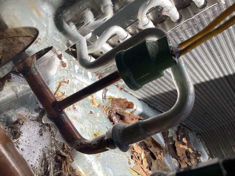 Responded to no cooling complaint on 8-month-old air conditioning system experiencing inadequate temperature reduction. Upon inspection, found unit operating with low refrigerant charge. Performed comprehensive leak detection procedures and identified active refrigerant leak at condensing coil. Photographic documentation captured severe corrosion on copper tubing with visible oxidation and surface degradation, along with frost accumulation on coil fins indicating restricted airflow and moisture exposure issues. Drain pan showed significant staining, organic debris accumulation, and evidence of prolonged moisture exposure. Temporarily recharged system to restore immediate cooling function; however, advised that this is a short-term solution as refrigerant will continue leaking. Strongly recommended immediate condensing coil replacement or full unit replacement given the age of equipment and severity of coil deterioration. Unit requires urgent attention to prevent complete system failure